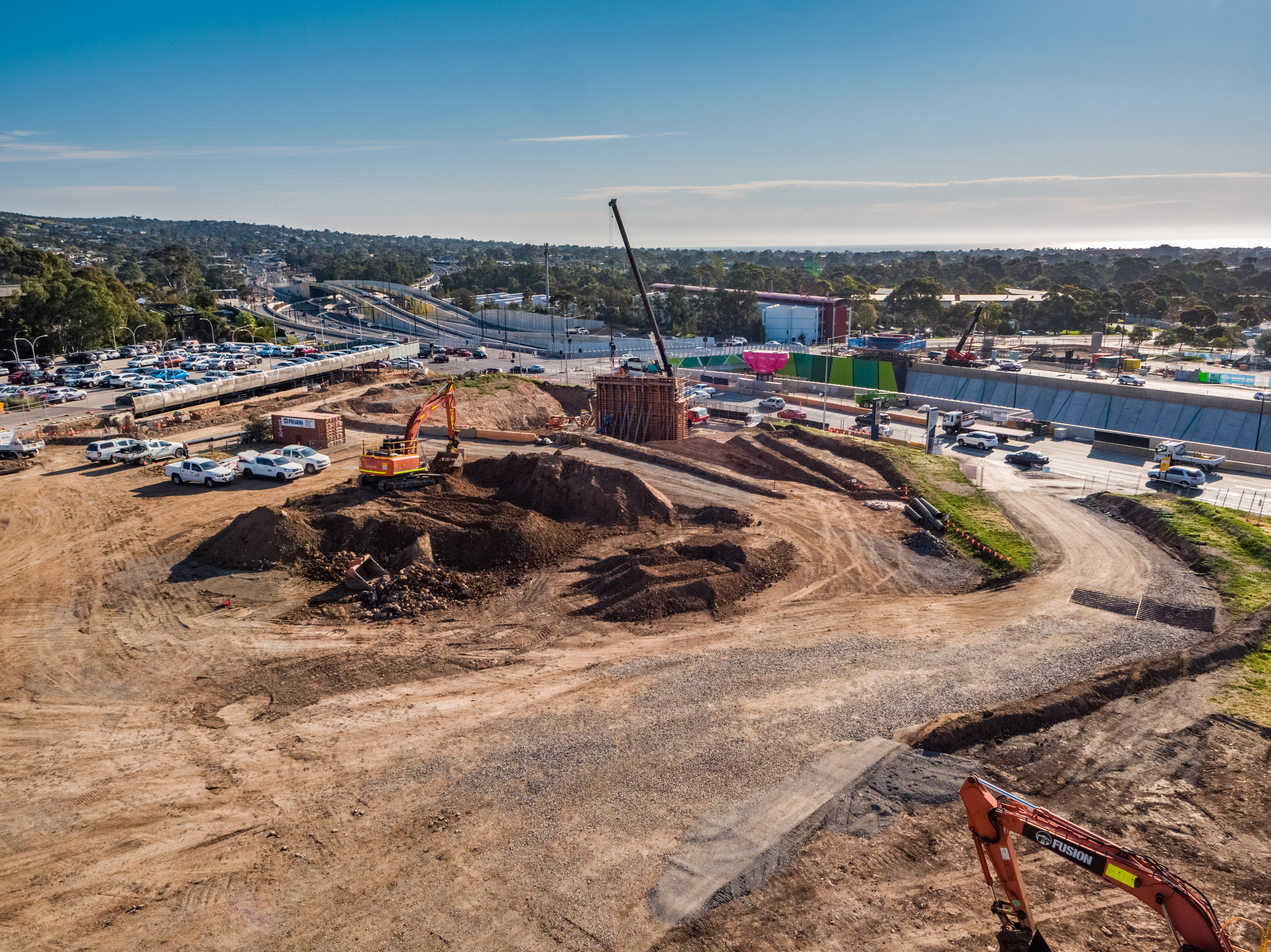 Earthworks are in the foreground, leading to a large structure, which is the first pier of the project. There is a crane behind it and other machinery, including an excavator in the foreground.