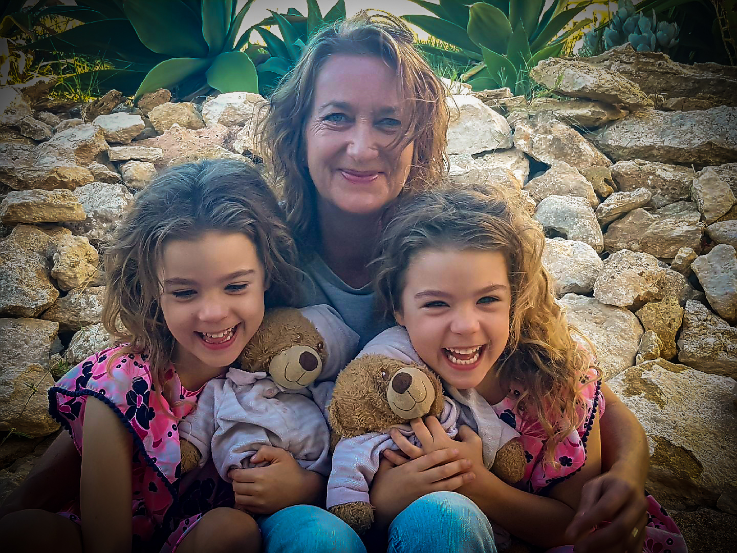 Picture of Paula Penny with her twin granddaughters smiling and holding their teddy bears 