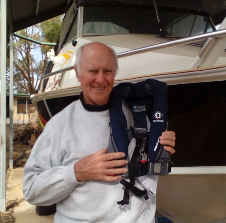 A man holding a horse collar while standing in front of a boat.