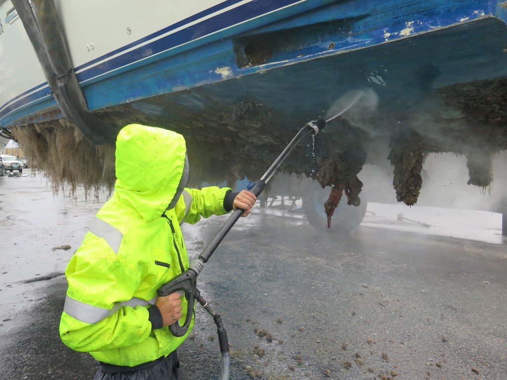 Man with high pressure water hose cleaning the bottom of a yacht